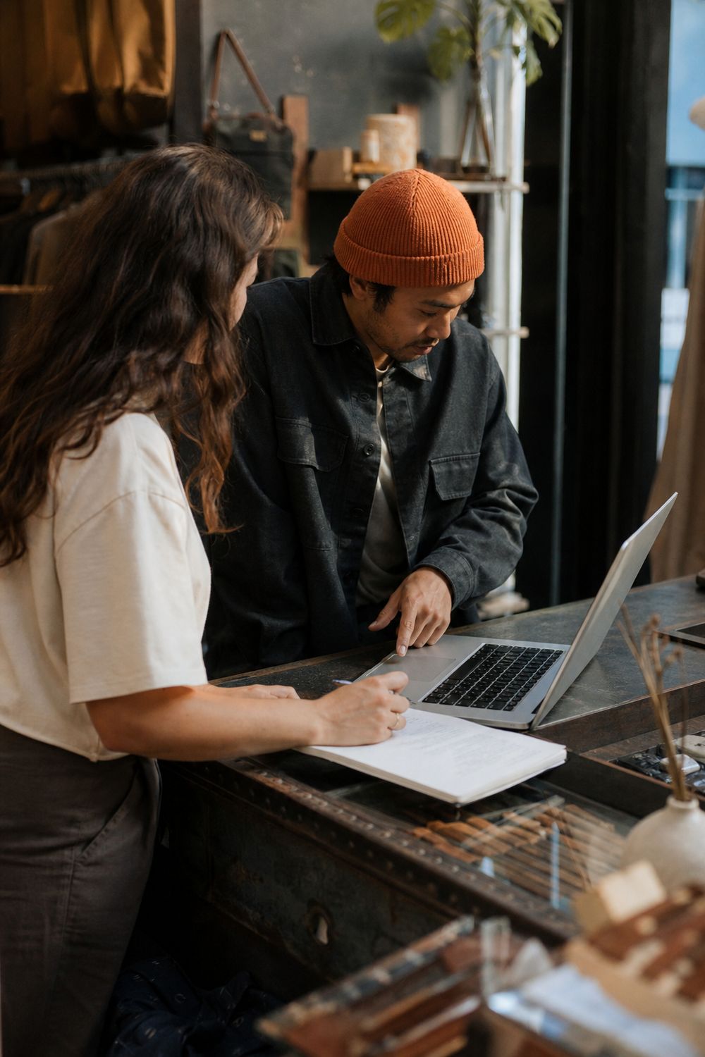 Two people at a shop counter walking through how work comes in on a laptop