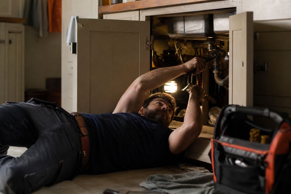 Plumber working under a kitchen sink with a wrench